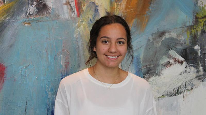 澳门足彩app intern Camila Moreno smiling in front of colorful artwork.