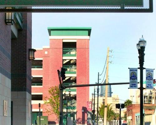 Exterior photo of Jacksonville 市政 Garages. Photo is through a doorway outside the arena. 街道两旁都是树木. Red brick with green trim accent the garage. Sign above doorway reads 'Exit 首页 Plate Gate'.